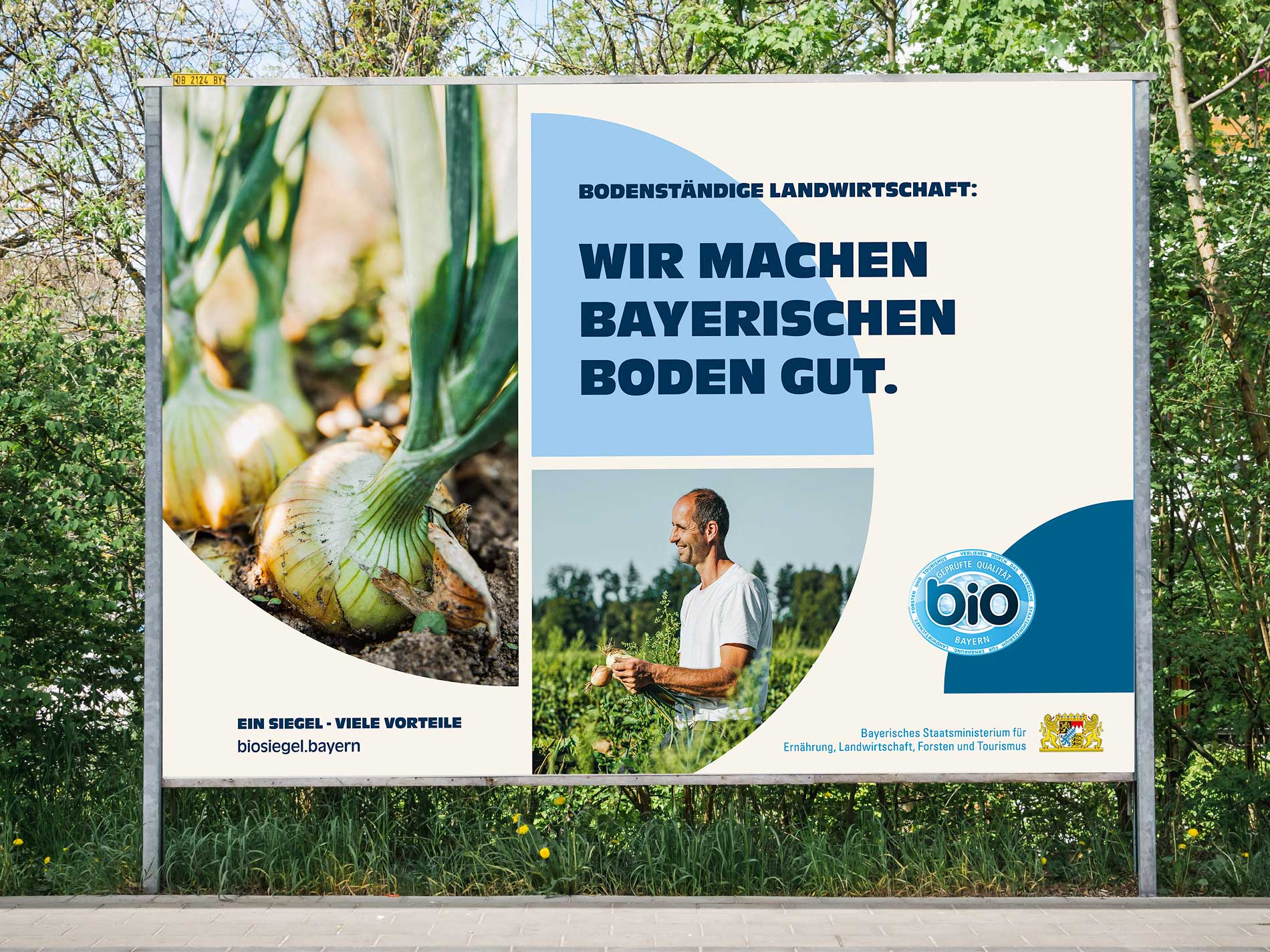 Großes Werbeplakat für das Bayerische Bio-Siegel an einer Straße. Links sind Zwiebeln in fruchtbarer Erde zu sehen, rechts ein Landwirt auf dem Feld. Der Slogan „Wir machen bayerischen Boden gut.“ hebt die nachhaltige Landwirtschaft hervor.