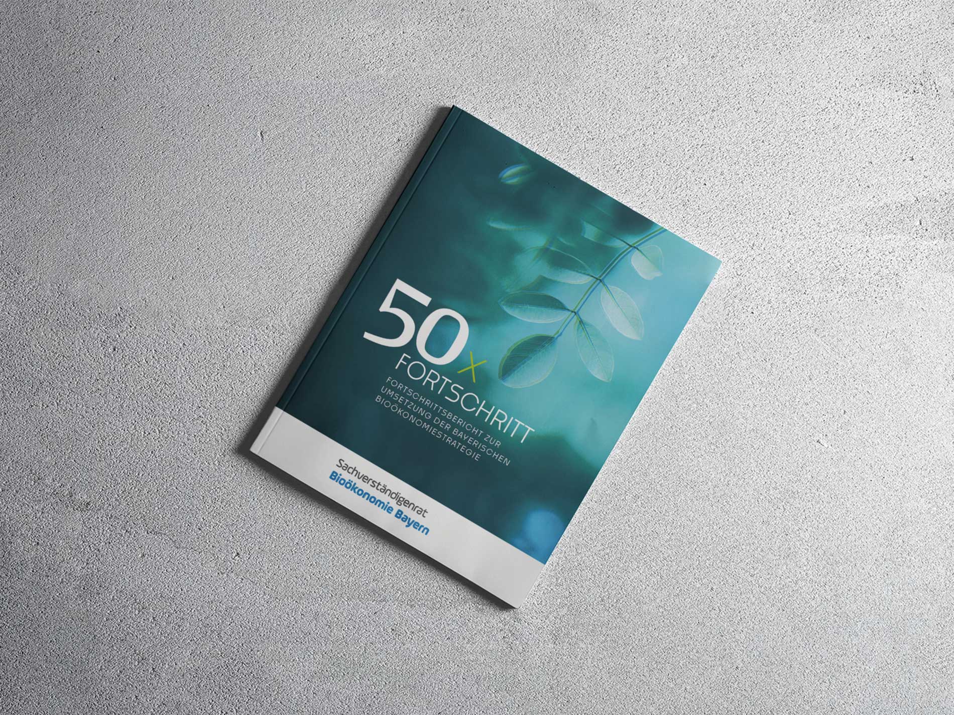 Das Bild zeigt den Fortschrittsbericht mit dem Titel "50 x Fortschritt" auf einem grauen Untergrund, die sich mit der Umsetzung der Bioökonomiestrategie in Bayern befasst.
