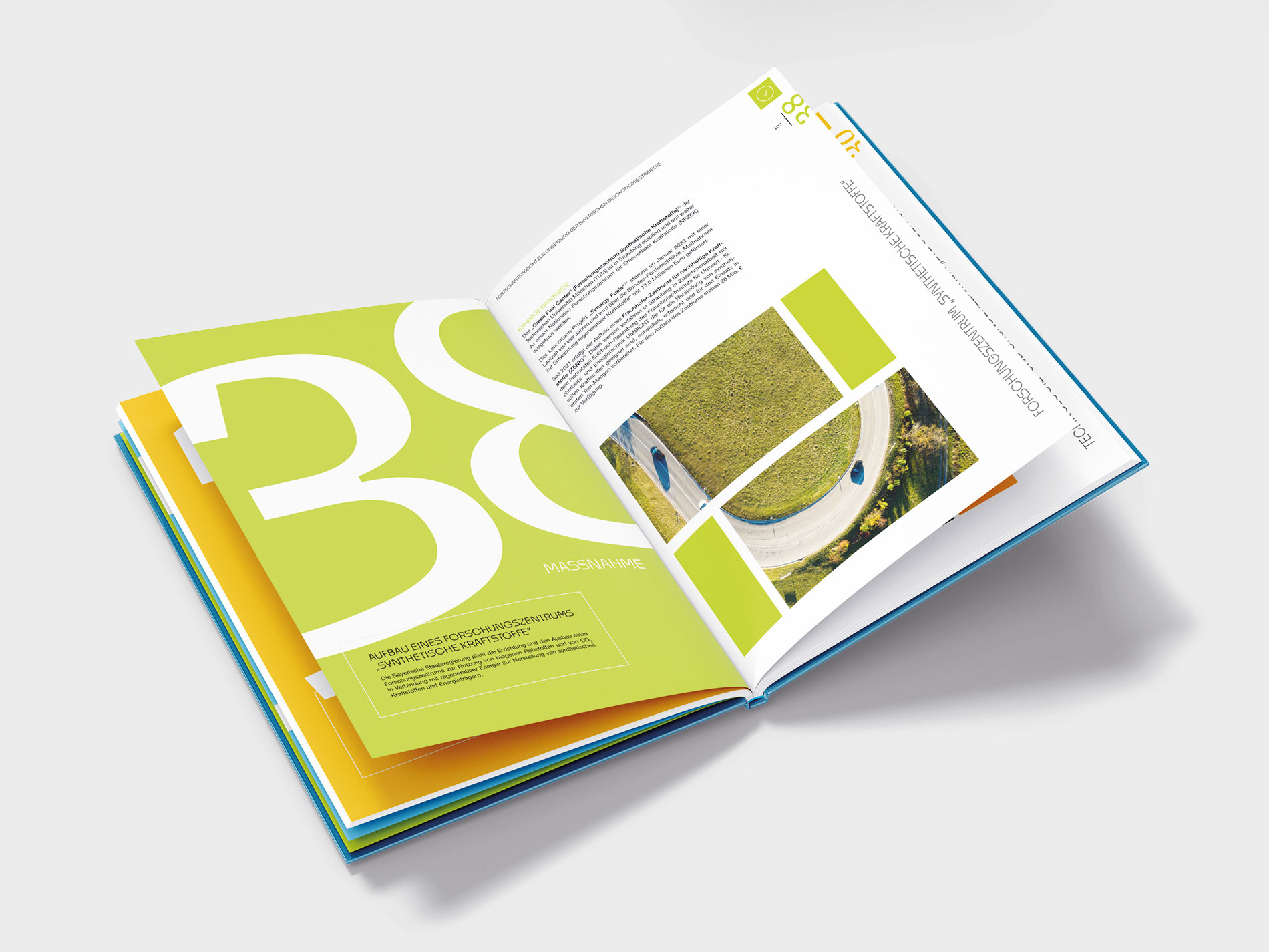 Das Bild zeigt eine Broschüre mit farbenfrohen Seiten in Gelb, Grün und Blau. Auf der linken Seite ist eine große "38" in Weiß auf grünem Hintergrund zu sehen, darunter der Text "Maßnahme: Aufbau eines Forschungszentrums 'Synthetische Kraftstoffe'". Auf der rechten Seite sind mehrere Luftaufnahmen einer Straße sowie weitere Textinformationen abgebildet. Die Gestaltung wirkt modern und professionell, mit einem Fokus auf klare Linien und kräftige Farben.