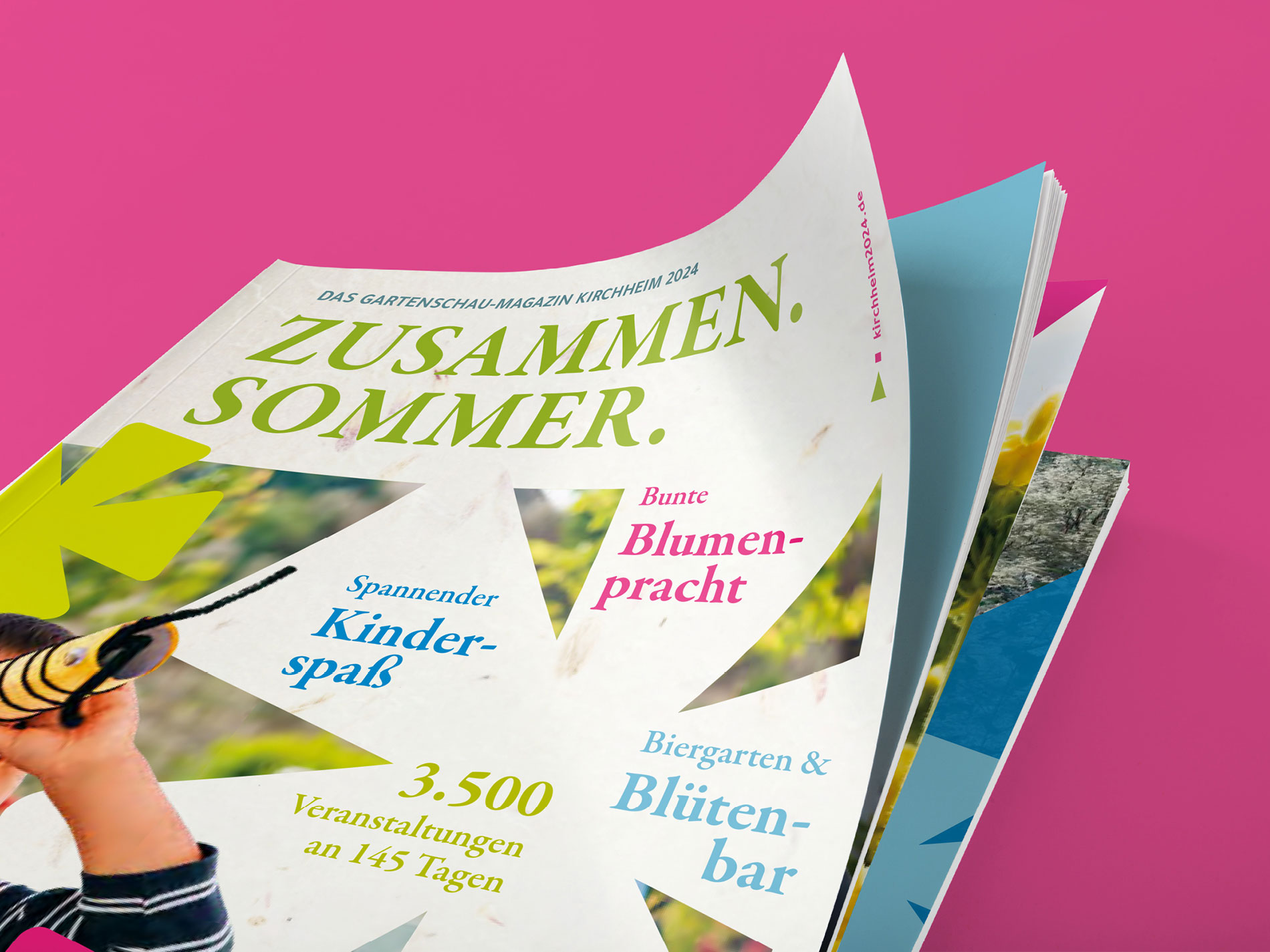 Das Bild zeigt ein aufgeschlagenes Magazin mit dem Titel "Zusammen. Sommer." und Ankündigungen wie "Spannender Kinderspaß", "Bunte Blumenpracht" und "Biergarten & Blütenbar", das auf einem pinkfarbenen Hintergrund liegt.