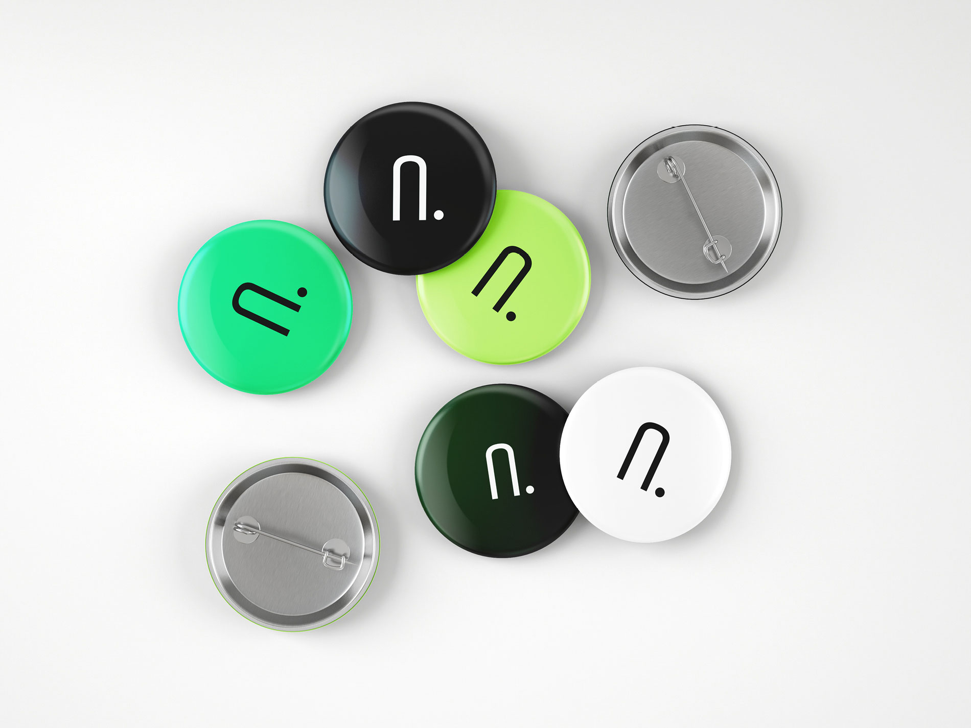 Das Bild zeigt mehrere Neuland Ansteckbuttons in verschiedenen Grüntönen sowie Schwarz und Weiß, die jeweils mit einem stilisierten "n." bedruckt sind.