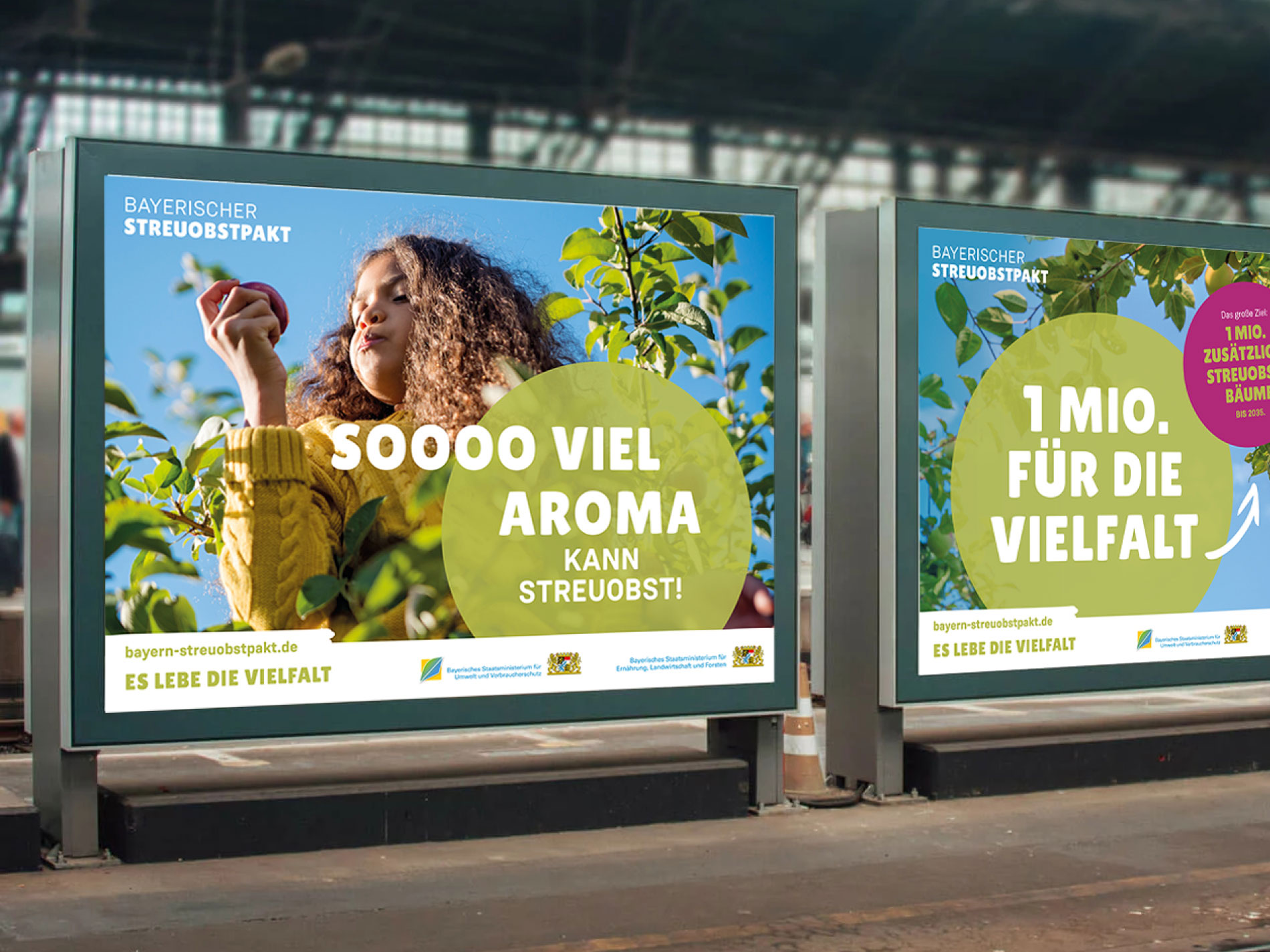 Das Bild zeigt zwei Werbetafeln in einer öffentlichen Umgebung, die für den Bayerischen Streuobstpakt werben, mit den Slogans "Soooo viel Aroma kann Streuobst!" und "1 Mio. für die Vielfalt", die auf die Förderung von Streuobstwiesen hinweisen.