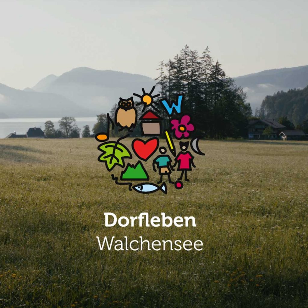 Blick auf eine Wiese mit Bäumen und Bergen im Hintergrund, darüber ein buntes Logo mit Symbolen wie Herz, Blume, Fisch, Eule und Haus sowie dem Text „Dorfleben Walchensee“.