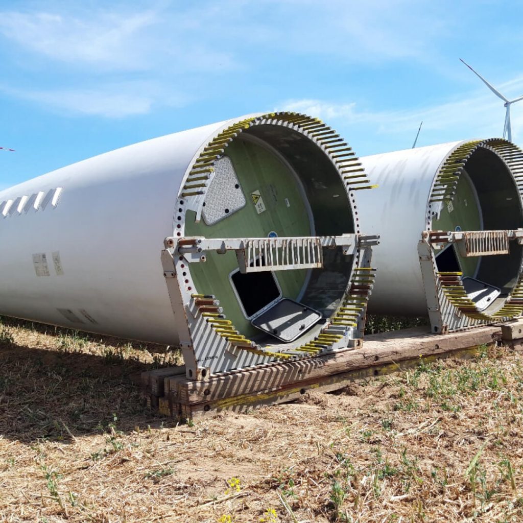 Zwei Turmsegmente einer Windkraftanlage liegen zur Montage bereit auf einem Feld unter blauem Himmel.