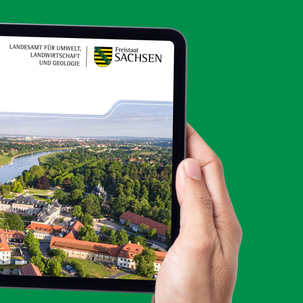 Hand hält ein Tablet mit der Titelseite einer LfULG-Publikation und einer Luftaufnahme mit Schloss Pillnitz und Elbe.